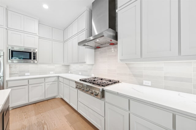 kitchen featuring white cabinetry, stainless steel appliances, wall chimney range hood, and light hardwood / wood-style floors