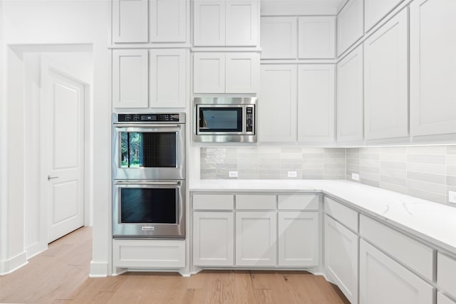 kitchen with white cabinetry, light stone counters, decorative backsplash, appliances with stainless steel finishes, and light wood-type flooring