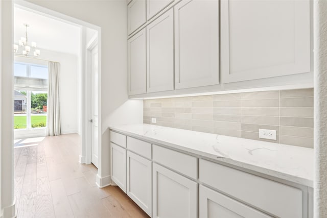 kitchen with decorative backsplash, light hardwood / wood-style floors, light stone countertops, and white cabinetry