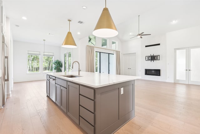 kitchen with ceiling fan, sink, decorative light fixtures, light hardwood / wood-style floors, and an island with sink