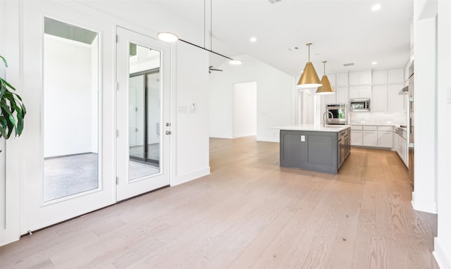 kitchen featuring stainless steel microwave, white cabinets, hanging light fixtures, an island with sink, and light hardwood / wood-style floors