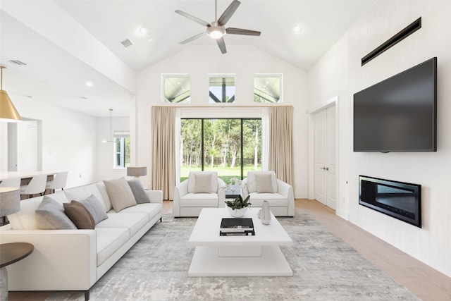 living room with ceiling fan, a large fireplace, high vaulted ceiling, and light hardwood / wood-style flooring