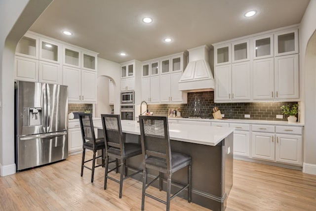 kitchen featuring a kitchen breakfast bar, custom range hood, white cabinets, a kitchen island with sink, and stainless steel appliances