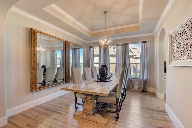 dining area featuring a tray ceiling, crown molding, a notable chandelier, and light wood-type flooring