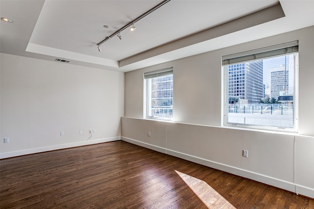 empty room featuring rail lighting, dark wood-type flooring, and a tray ceiling