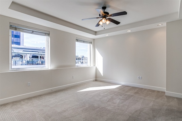 carpeted spare room with ceiling fan and a raised ceiling