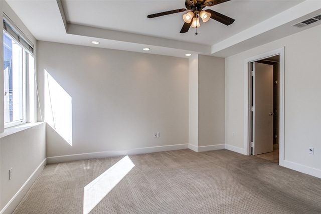 carpeted spare room with ceiling fan, a raised ceiling, and a wealth of natural light