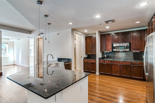 kitchen with sink, hanging light fixtures, stainless steel appliances, light hardwood / wood-style flooring, and dark stone countertops