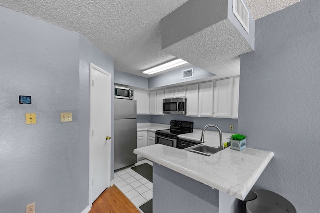 kitchen with light tile floors, sink, white cabinetry, stainless steel appliances, and kitchen peninsula