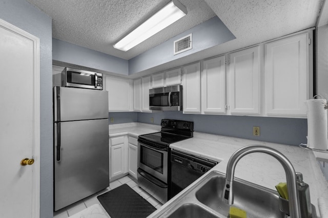 kitchen featuring appliances with stainless steel finishes, light tile floors, a textured ceiling, sink, and white cabinetry