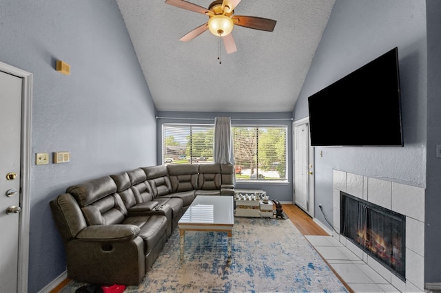 living room featuring ceiling fan, lofted ceiling, a textured ceiling, a tile fireplace, and light wood-type flooring