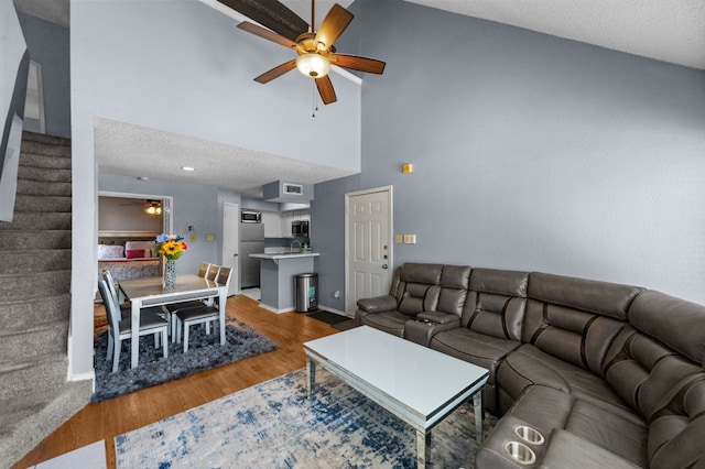 living room with hardwood / wood-style floors, high vaulted ceiling, ceiling fan, and a textured ceiling