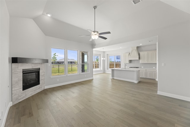 unfurnished living room featuring lofted ceiling, sink, a tiled fireplace, ceiling fan, and light hardwood / wood-style floors