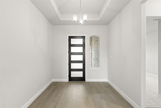 entryway with an inviting chandelier, light hardwood / wood-style floors, and a tray ceiling