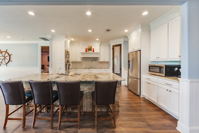 kitchen featuring appliances with stainless steel finishes, a large island with sink, dark hardwood / wood-style flooring, light stone countertops, and white cabinets