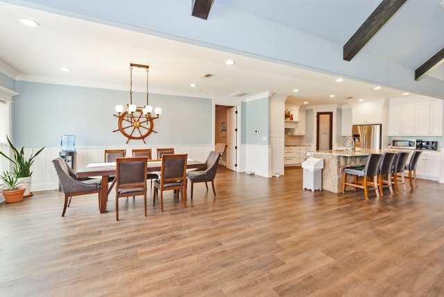 dining room featuring light hardwood / wood-style floors, sink, ornamental molding, beam ceiling, and an inviting chandelier