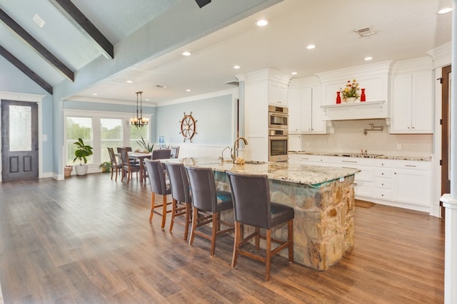 kitchen featuring dark wood-type flooring, light stone counters, double oven, white cabinetry, and lofted ceiling with beams