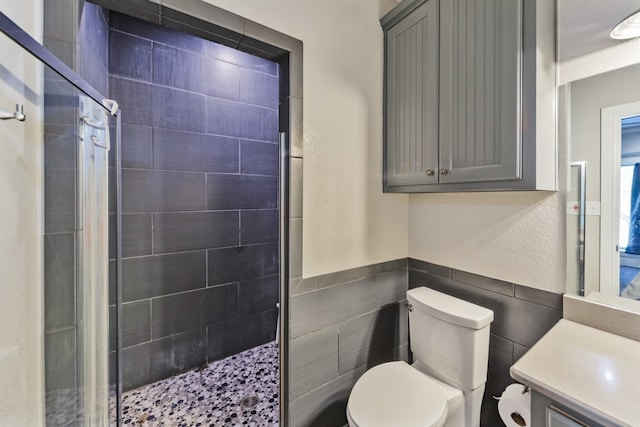 bathroom featuring vanity, toilet, a tile shower, and tile walls