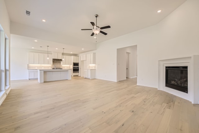 unfurnished living room with ceiling fan, sink, and light hardwood / wood-style flooring