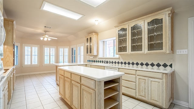 kitchen with light tile patterned flooring, kitchen peninsula, a kitchen island, light brown cabinets, and ceiling fan