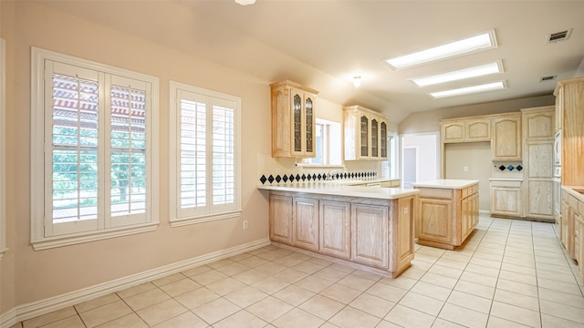 kitchen featuring light brown cabinets, backsplash, light tile patterned floors, and a center island