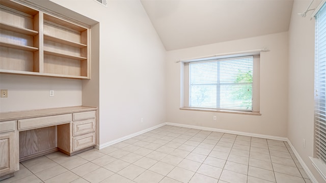 unfurnished office with lofted ceiling, built in desk, and light tile patterned floors