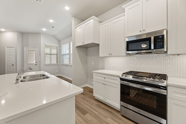 kitchen featuring backsplash, sink, light wood-type flooring, vaulted ceiling, and stainless steel appliances