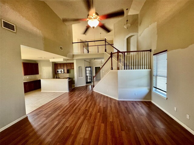 unfurnished living room featuring ceiling fan, a towering ceiling, and dark hardwood / wood-style flooring