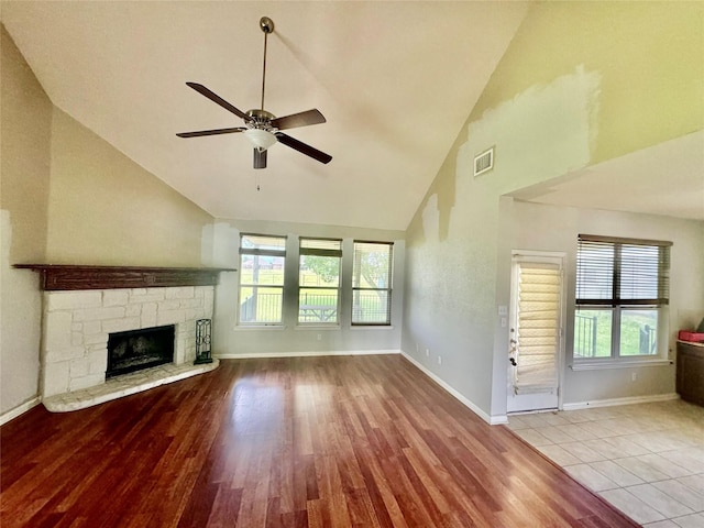 unfurnished living room with a stone fireplace, light hardwood / wood-style flooring, high vaulted ceiling, and ceiling fan