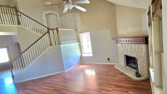 unfurnished living room with hardwood / wood-style floors, a stone fireplace, ceiling fan, and a high ceiling