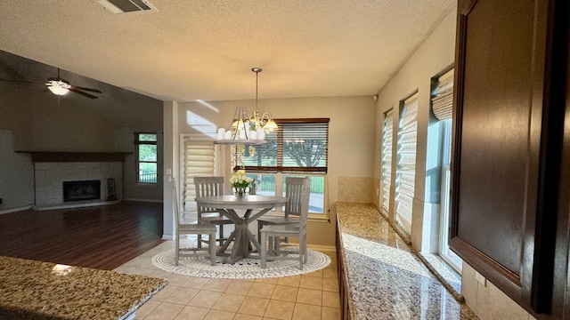 dining room featuring light tile patterned flooring, plenty of natural light, a fireplace, and a textured ceiling