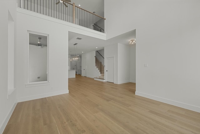 unfurnished living room featuring a high ceiling, light wood-type flooring, and an inviting chandelier