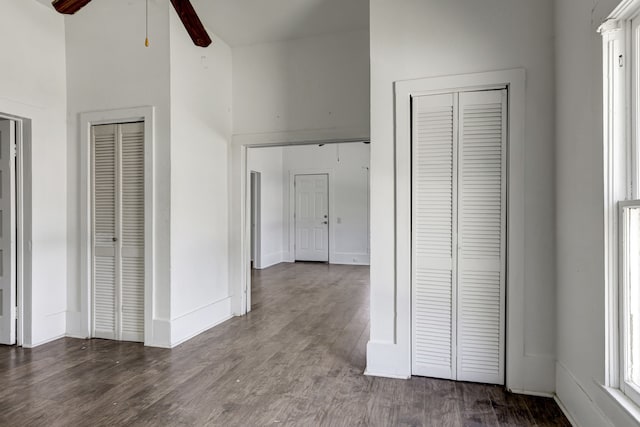 unfurnished bedroom with two closets, ceiling fan, and dark hardwood / wood-style flooring