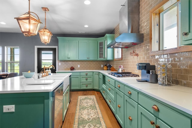 kitchen featuring a center island with sink, light countertops, light wood-style flooring, a sink, and wall chimney range hood