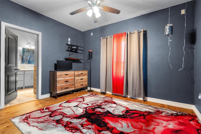 bedroom featuring a ceiling fan, baseboards, ensuite bath, and wood finished floors