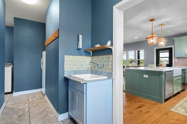 kitchen with tasteful backsplash, dishwasher, light countertops, green cabinets, and a sink