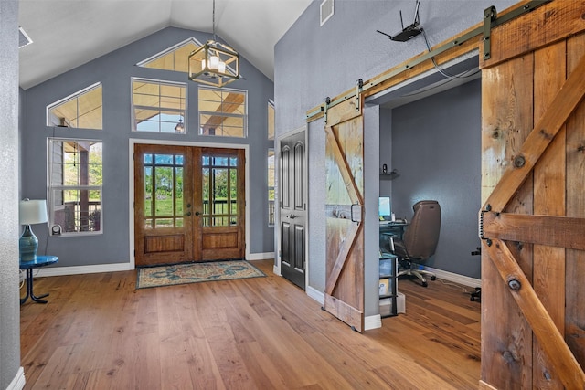 foyer featuring french doors, hardwood / wood-style floors, a barn door, high vaulted ceiling, and baseboards