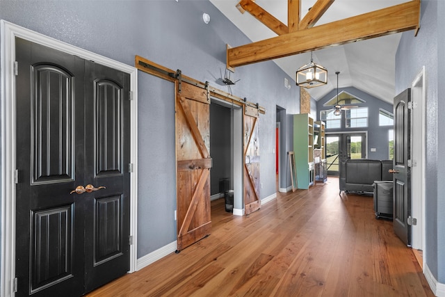 entrance foyer featuring a barn door, hardwood / wood-style floors, high vaulted ceiling, beamed ceiling, and ceiling fan