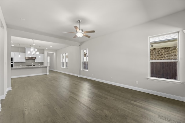 unfurnished living room featuring ceiling fan with notable chandelier and dark hardwood / wood-style flooring