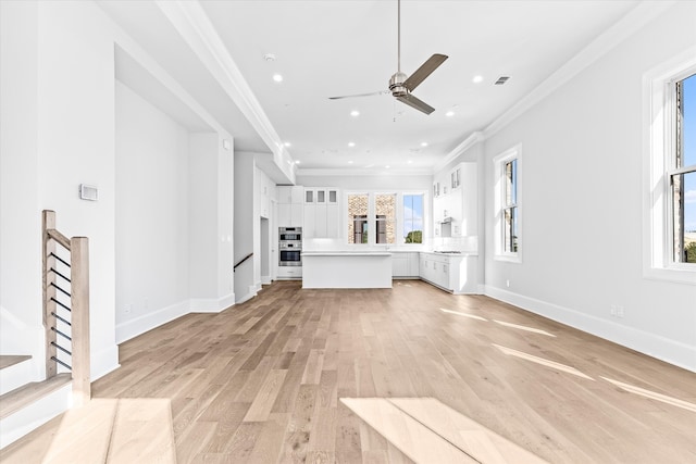 unfurnished living room with ornamental molding, ceiling fan, light wood-type flooring, and plenty of natural light