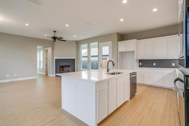 kitchen featuring backsplash, ceiling fan, a center island with sink, sink, and stainless steel dishwasher