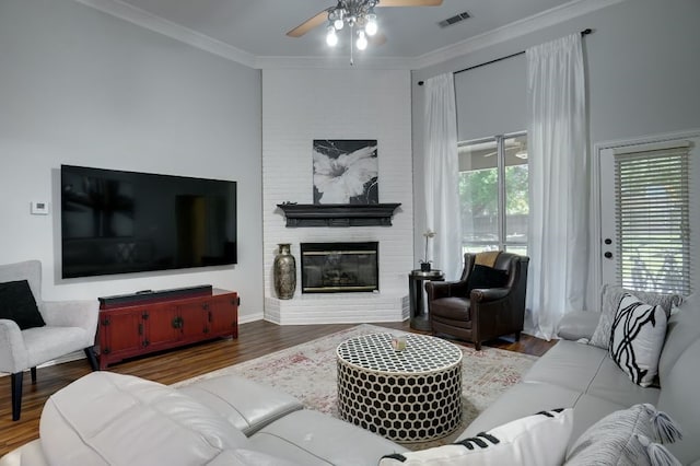 living room featuring ceiling fan, dark wood-type flooring, crown molding, and a brick fireplace