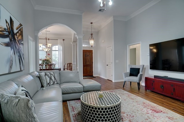 living room featuring dark hardwood / wood-style floors, a notable chandelier, crown molding, and decorative columns