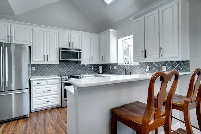 kitchen featuring appliances with stainless steel finishes, vaulted ceiling, white cabinetry, and a kitchen bar