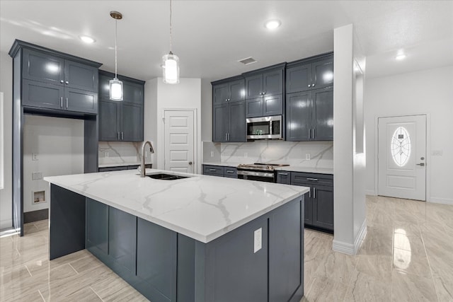 kitchen with light stone counters, a kitchen island with sink, sink, pendant lighting, and appliances with stainless steel finishes