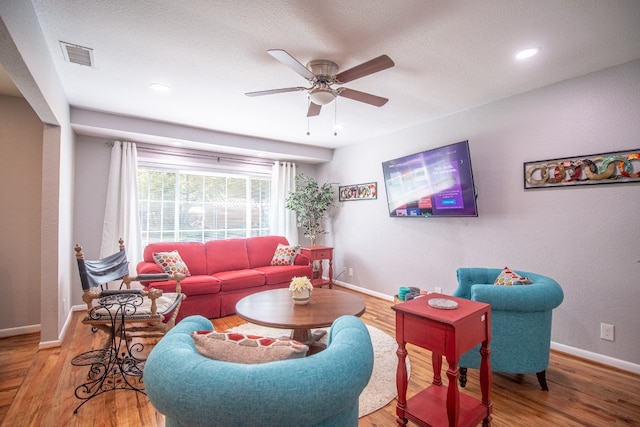 living room with a textured ceiling, ceiling fan, and light hardwood / wood-style floors