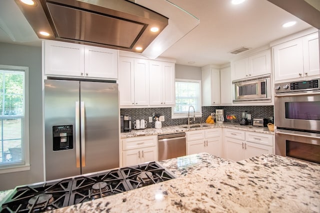 kitchen with light stone countertops, stainless steel appliances, tasteful backsplash, white cabinets, and sink