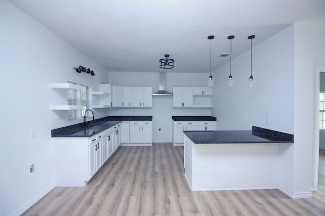 kitchen featuring white cabinets, wall chimney exhaust hood, light hardwood / wood-style flooring, decorative light fixtures, and sink