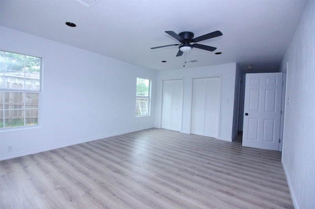 unfurnished bedroom with light hardwood / wood-style flooring, multiple closets, multiple windows, and ceiling fan