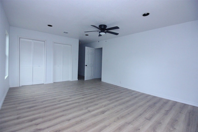 unfurnished bedroom featuring ceiling fan, multiple closets, and light hardwood / wood-style flooring